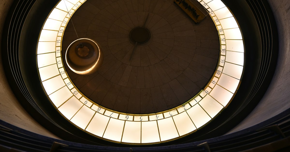 A Foucault pendulum swinging above a circular floor ringed with numbered lights.